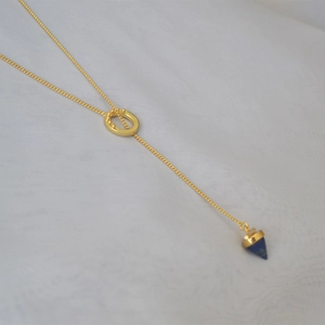 Detail of brass lariat necklace featuring a blue lapis lazuli cone pendant on white fabric