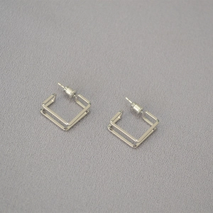 Macro view of geometric double-layered square stud earrings in polished silver finish