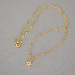 Detail of gold star pendant with white enamel and pink zircon on a fine chain