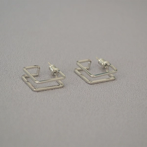 Close-up of geometric square double-layer silver metal stud earrings on grey fabric
