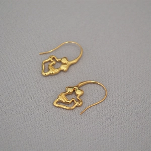 Macro shot of gold-plated skull hook earrings with a textured vintage punk finish
