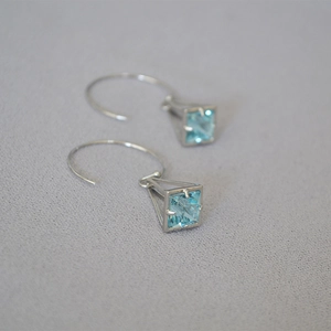 Macro detail of geometric cage drop earrings with light blue zircon and silver finish