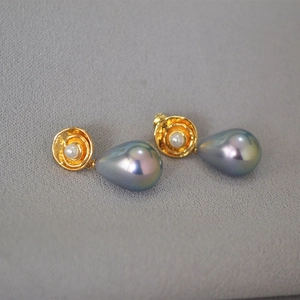 Close-up of golden floral stud earrings with large iridescent grey teardrop pearls
