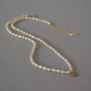 Detailed macro of rice pearl necklace featuring a golden evil eye pendant with blue crystals