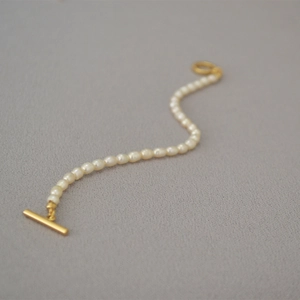 Detail of irregular freshwater pearl bracelet with golden toggle clasp on dark background