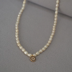 Detail of freshwater pearl necklace featuring a blue evil eye pendant with gold plating