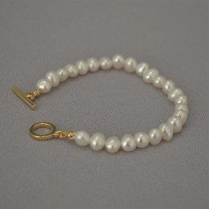 Detail of freshwater seed pearl bracelet with a golden OT toggle clasp on grey fabric