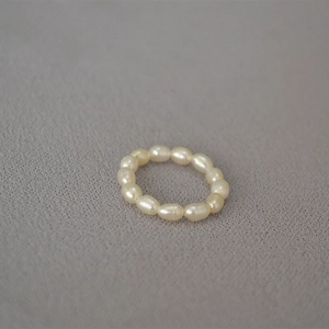 Detailed shot of white freshwater rice pearl elastic ring on grey fabric texture