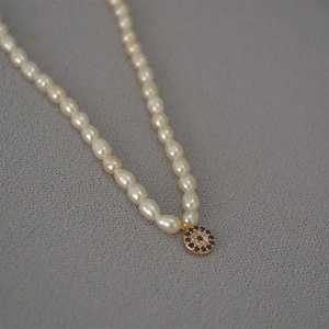 Detail of freshwater pearl necklace featuring a blue evil eye pendant with gold accents