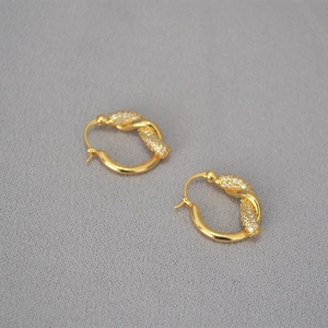 Dettaglio di orecchini a cerchio placcati oro con design a nodo e pavé di cristalli