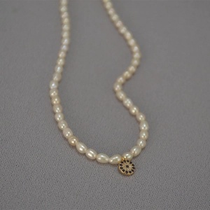French retro necklace with freshwater pearls and gold evil eye pendant on grey fabric