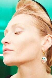 Detail of baroque pearl drop earring with quirky face charm and green gem eyes