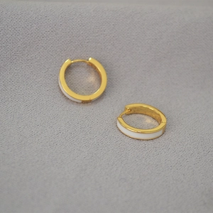 Détail de boucles d'oreilles créoles dorées avec émail blanc sur tissu gris