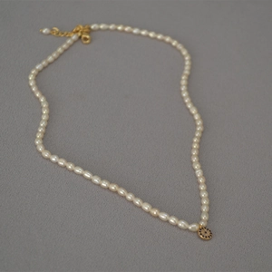 Macro shot of freshwater rice pearl necklace featuring a blue evil eye gold pendant detail