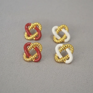 Detail view of red and cream enamel interlocking rope knot stud earrings on sand surface