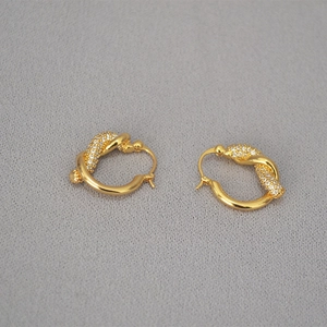 Dettaglio di orecchini a cerchio intrecciati placcati oro con pavé di zirconi