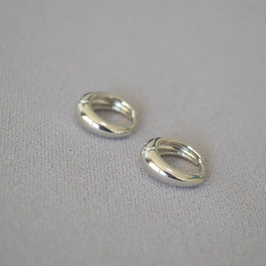 Détail des boucles d'oreilles créoles argentées avec finition miroir polie sur tissu gris