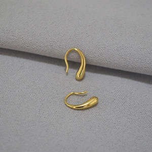 Makroaufnahme goldener tropfenförmiger Ohrringe mit elegantem Haken auf grauem Hintergrund