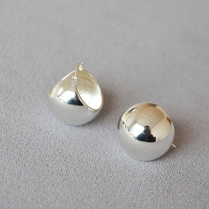 Macro view of polished silver-plated dome earrings on textured fabric background