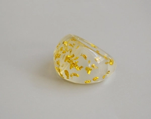 Detailed macro view of handmade transparent resin ring with embedded gold leaf foil flakes