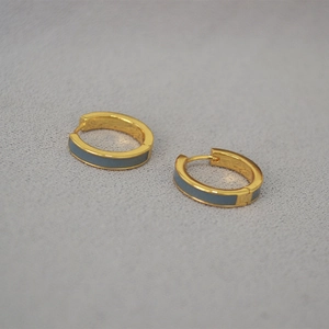 Détail de boucles d'oreilles dorées avec émail gris et finition en métal poli