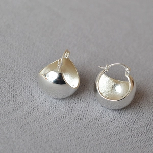 Macro shot of minimalist polished silver U-shape hoop earrings on textured grey fabric