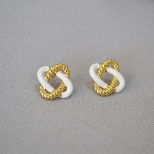 Close-up of golden twisted rope and white enamel knot stud earrings on gray background