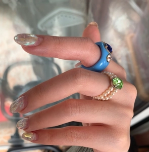 Close-up of resin ring with blue zircon and double-row pearl ring with green gemstone