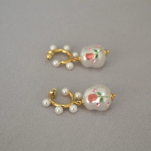 Detailed macro of vintage pearl earrings with red rose pattern and pink crystals