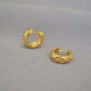 Detailed close-up of gold-plated quilted pattern hoop earrings on a grey textured fabric
