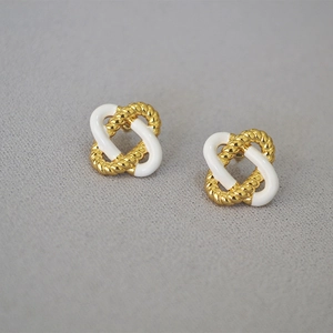 Elegant gold knot earrings with white enamel and twisted texture on a gray surface