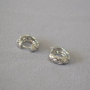Close-up of silver quilted texture hoop earrings with minimalist lattice design