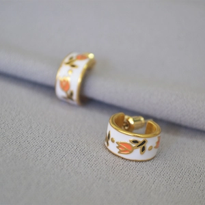 Macro detail of tulip flower pattern on brass gold plated enamel C-shaped hoop earrings