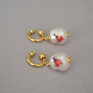 Detail of baroque pearl drop earrings featuring red heart graffiti and golden metal hoops