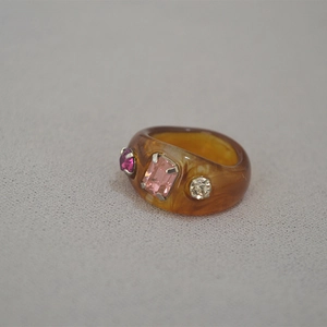 Close-up of amber resin ring featuring three colorful rhinestones in metal claw settings