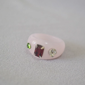 Detailed view of pink resin ring featuring inlaid green, red, and white crystals