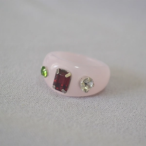 Macro shot of pink resin ring featuring inlaid red, green, and clear sparkling gemstones