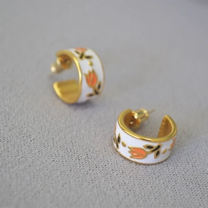 Detailed view of C-shape brass earrings featuring orange tulips and white enamel finish