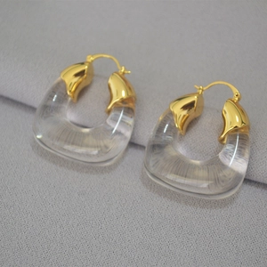 Detail of U-shaped gold-plated resin earrings with clear texture on grey fabric