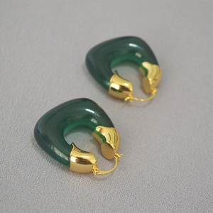 Macro detail of U-shaped green resin earrings with polished gold-plated metal caps