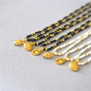 Detail of beaded necklaces with gold shell pendants in black and white styles