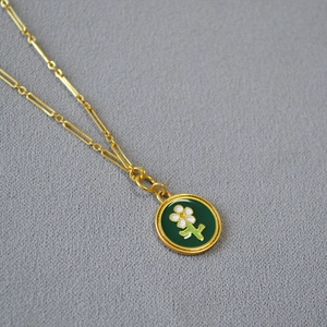 Détail du collier doré avec pendentif rond en émail vert et motif de petite fleur blanche