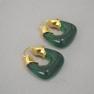 Detail of U-shaped gold-plated earrings with dark green translucent resin inserts