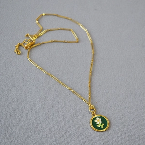 Détail de la chaîne trombone dorée et du pendentif floral en émail vert foncé