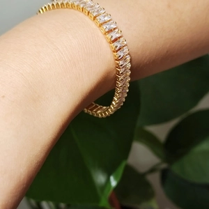 Bracelet tennis doré serti de zircons taille baguette porté sur un fond de feuilles vertes