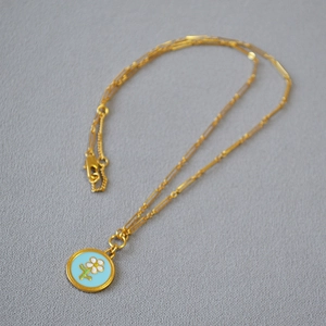 Détail d'un collier chaîne dorée avec un pendentif floral en émail bleu clair
