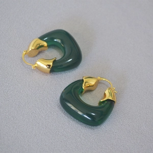 Detail of C-shaped hoop earrings featuring green translucent resin and gold-plated metal
