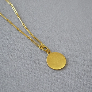 Détail du collier doré avec maillons longs et pendentif rond lisse de style minimaliste