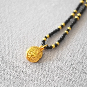 Macro view of gold seashell pendant with intricate carvings on black beaded necklace