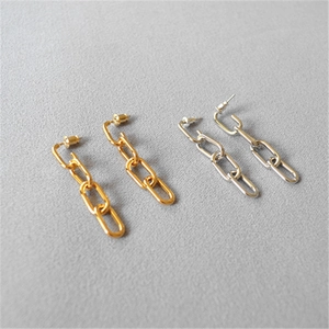 Close-up of industrial style triple-link chain drop earrings in gold and silver finish